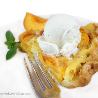 Peach custard pie on a white plate with a scoop of vanilla ice cream on top