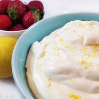 Lemon cream with lemon curd and strawberries in a small blue bowl garnished with lemon zest